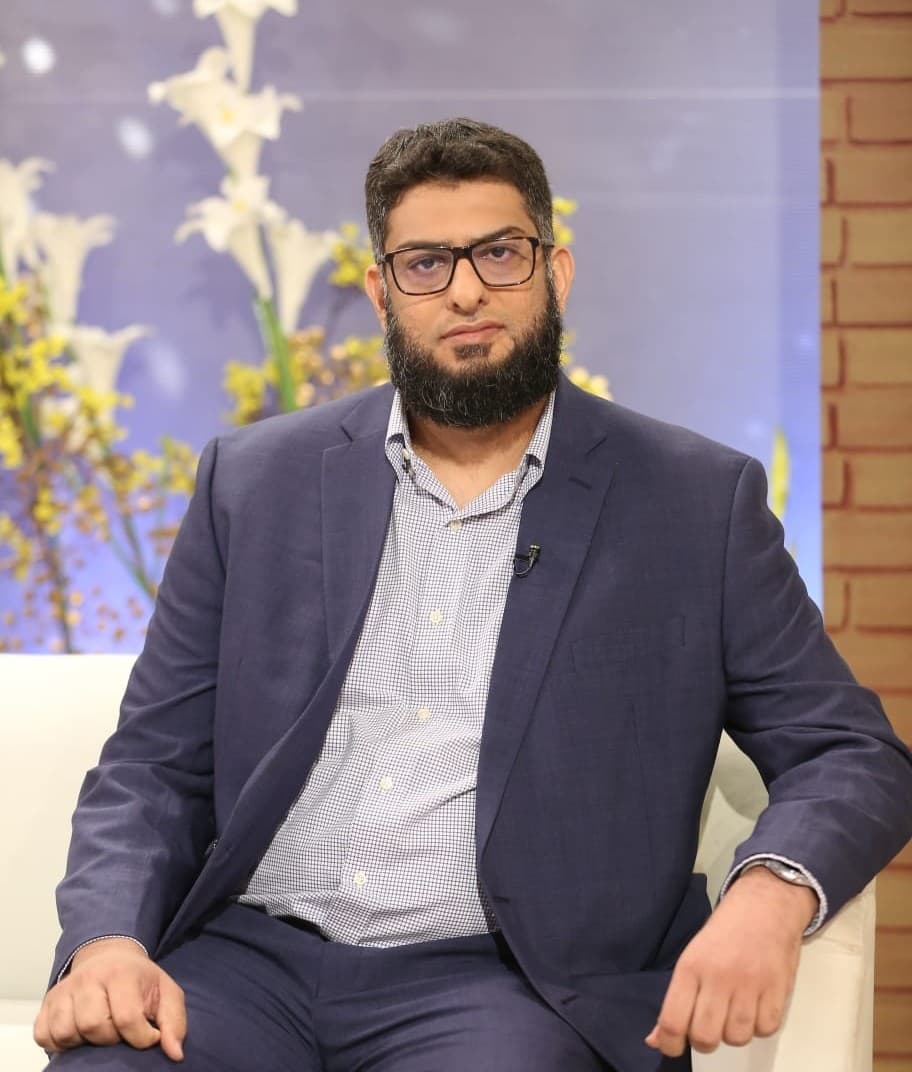 Dr. Zeeshan Malik in a navy suit, seated for a television interview